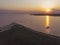 Aerial Drone Shot of colorful pink lake at sunset time with wind turbines farm on background. Cinematic landscape view