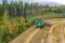 Aerial drone shot of combine harvester in action on small wheat field side, unloading grains. Pine tree forest at side, back view