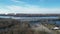 Aerial drone stationary view above bear trees of a highway bridge over water with steam coming from factories in the distance