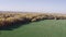 Aerial drone view of beautiful field, lush calm autumn mixed forest and blue sky. Farm life scenery, idyllic countryside