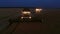 Aerial drone view of the combine harvester with lights works in night wheat fields.