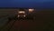 Aerial drone view of the combine harvester with lights works in night wheat fields.