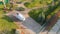 Aerial drone view of covered boat parked on trailer at backyard garden with circle path, green grass lawn hills and
