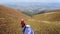 Aerial drone view of female hiker in red standing on top of mountain in summer near tent.