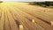 Aerial drone view of harvested mowed golden wheat field with many straw hay bales at warm sun sunset light on summer or