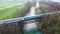 Aerial drone view of public train passing old metal bridge