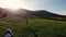 Aerial drone view of young happy woman run along grass near tent to say goodbye to sunset, and raises her hands up