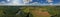 Aerial drone wide panoramic view on wind turbine, snake shape road, wheat fields and forest during summer