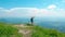 AERIAL: Ecstatic female hiker climbs a grassy mountain and lifts her arms in air