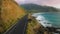 Aerial empty road along cinematic coastline, above dramatic rocky shore on Oahu