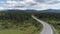 Aerial of the empty road going through forest, summer nature landscape. Scene. Flying above the highway through the