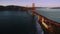 Aerial evening over San Francisco Bay toward and alongside Golden Gate bridge by sunset, boat crossing under the bridge