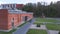 Aerial of the facade of red brick industrial building with green lawn and pedestrian walkways with a black car parked