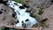 AERIAL. Female tourist standing on the bridge near huge waterfall. Woman looking to the springs mountains river, view