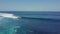 Aerial fly over a blue ocean with groups of surfers paddling the riding waves.