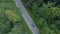 AERIAL: Flying above a car cruising through the beautiful dark green forest.