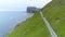 AERIAL: Flying behind a car cruising along a coastal road in Faroe Islands.