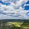 Aerial Flying over countryside with village, forest, ponds, and fields at summer time under dramatic cloudy sky with rays of the