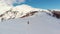 Aerial: flying over hiker walking towards snowy mountain top, ski touring mountaineering snow mountain, panoramic view on the alps