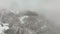 Aerial foggy landscape with mountain cliffs covered with fresh fallen snow during heavy snowfall in winter mountain