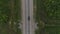 Aerial following shot of a black sedan car driving on an empty road surrounded by a summer forest