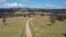 Aerial footage of a dirt road with white fence post markers in a green agricultural field