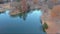 Aerial footage of a gorgeous blue lake surrounded by autumn colored trees and lush green trees and yellow winter grass