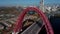 Aerial footage on modern urban red cable arch bridge with automobiles, cars on road above the river, amont park and city