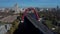 Aerial footage on modern urban red cable arch bridge with automobiles, cars on road above the river, amont park, city buildings