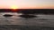 Aerial footage of a rock jetty beside a beach with a crowd of people gathered to watch the sunset.