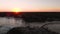 Aerial footage of a rock jetty beside a beach with a crowd of people gathered to watch the sunset.