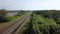 Aerial of four rows of long railways layng along green line of bushes and trees