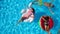 Aerial. Friends chilling in swimming pool with inflatable flamingo, swan, mattress. Happy young people bathe on floating