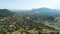 Aerial of golden hills covered by green bushes and trees and the coastal town on cloudy sky background. Shot. Flying