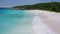 Aerial hover above ocean waves on tropical sandy beach. White sand, shallow turquoise lagoon water and lonely catamaran