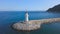 Aerial of lighthouse near the blue ocean. Art. White beautiful beacon with walking tourists and clear sky with the