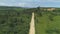 AERIAL: Lonely white van drives down tropical dirt road towards busy gravel pit.