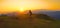 AERIAL: Mountain biker riding his bicycle up a grassy hill at picturesque sunset