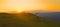 AERIAL: Mountain biker riding his bicycle up a grassy hill at picturesque sunset