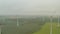 Aerial: multiple wind turbines on rich yellow agriculture field in fog rotating by the force of the wind and generating