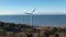 Aerial orbiting shot towards and around large spinning wind turbine. Calm blue sea in background