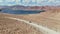 Aerial over off road 4x4 car driving along gravel trail path toward lake in arid mountains.Pamir Highway silk road