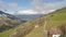 Aerial panorama of Alpine village on green mountain hills, cloudy sky, tourism