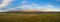 An aerial panorama of a large distant mountain under blue skies with interstate traffic moving in front of it and a large green