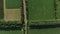 Aerial panorama of the road, that leads between green patterns of fields and gardens