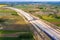 Aerial panorama top down view of an unfinished asphalt covered road with dirt, tracks of heavy machinery at construction site. The