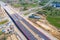 Aerial panorama top down view of an unfinished asphalt covered road with dirt, tracks of heavy machinery at construction site. The