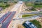 Aerial panorama top down view of an unfinished asphalt covered road with dirt, tracks of heavy machinery at construction site. The