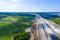 Aerial panorama top down view of an unfinished asphalt covered road with dirt, tracks of heavy machinery at construction site. The