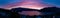 Aerial panoramic shot of a gorgeous purple sunset by the lake surrounded by mountains